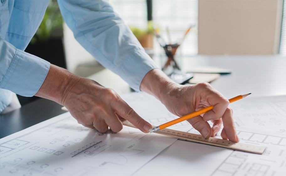 A man using a ruler to draw straight lines in a blueprint