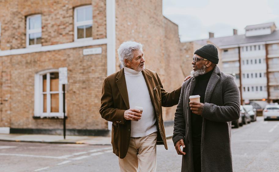 Two men walking on down an empty road with coffee’s in hand